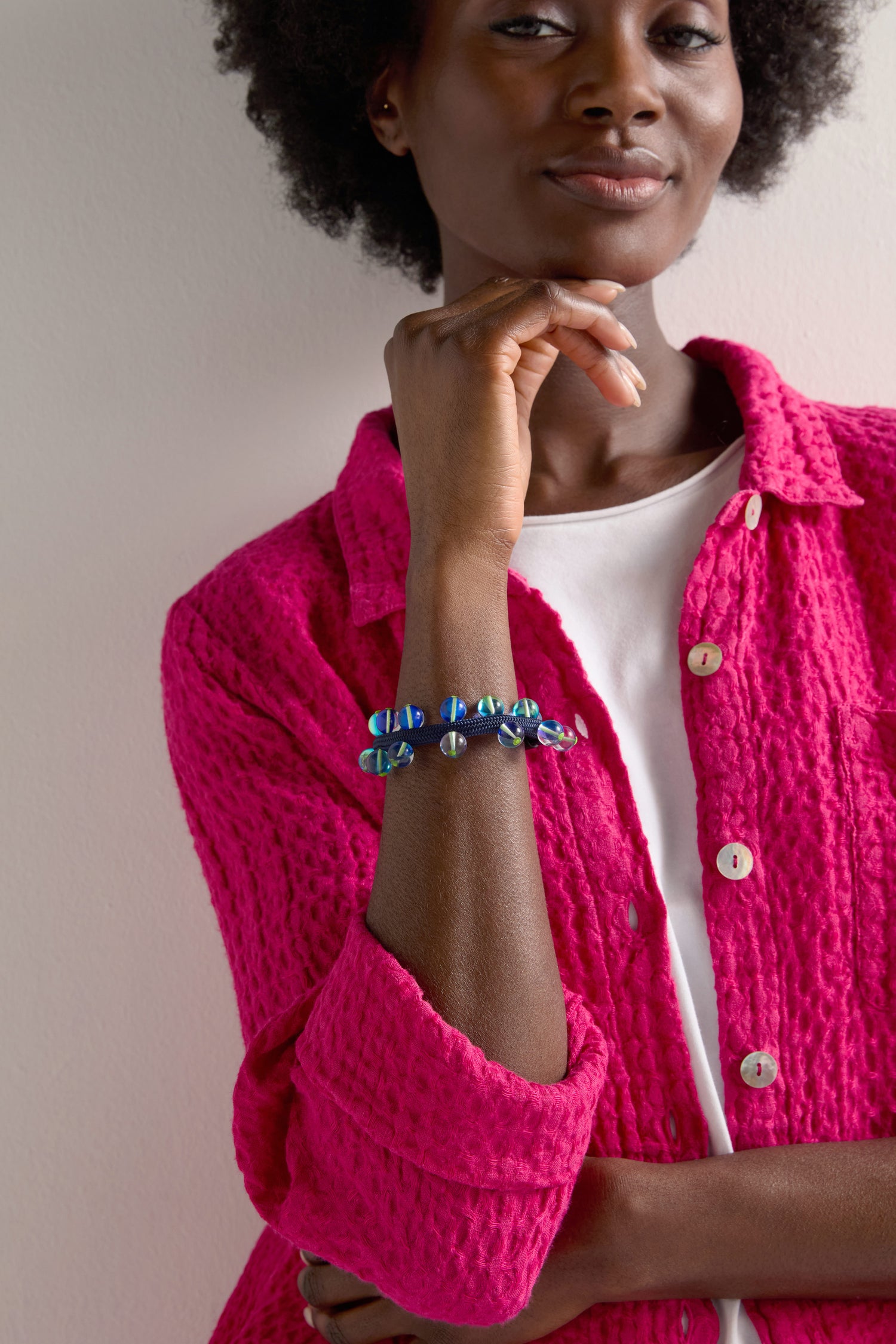 Clad in a bright pink textured jacket and white top, the person gazes forward with a slight smile against a light backdrop, showcasing the Atmosphere Bracelet.