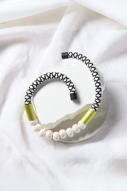 Two bracelets sit on a white background. One features a white and black braided band with gold and black ends; the other, showcasing a modern aesthetic, has a similar band with pearlescent ceramic beads for a striking look, reminiscent of the Milky Way Pearlescent Necklace.