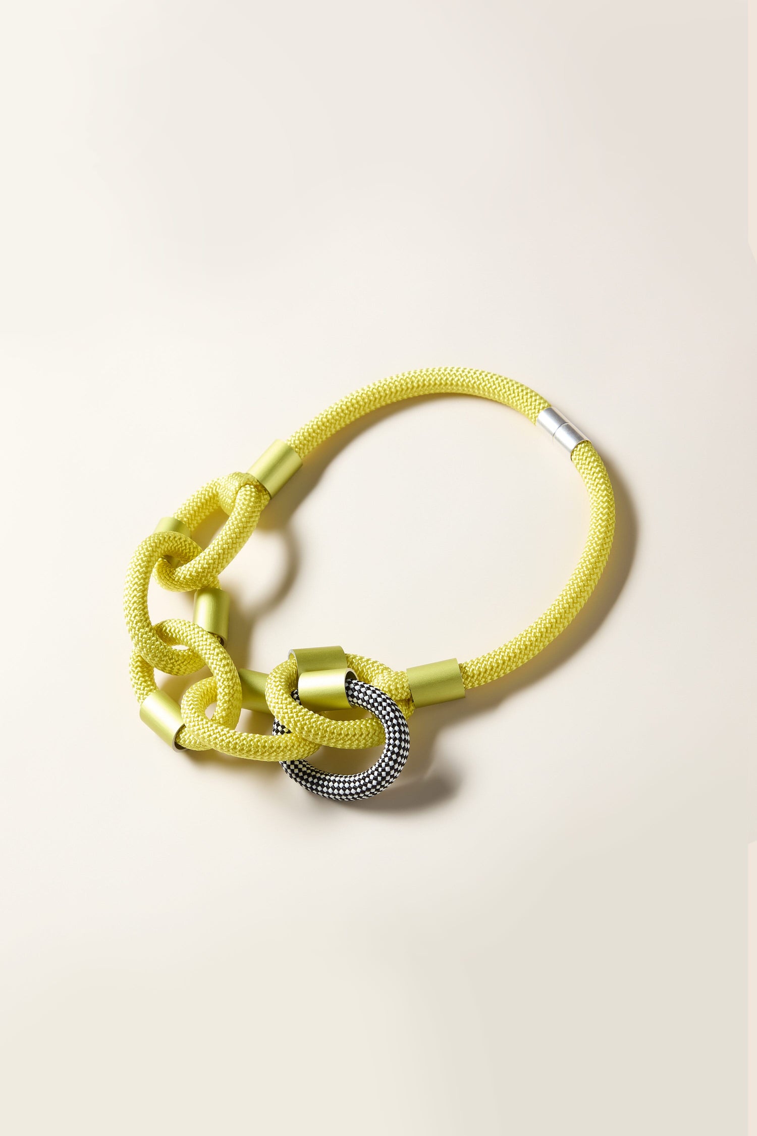 The Zig Zag Hoops Necklace by Christina Brampti showcases a yellow mesh chain adorned with large interlocking loops and accented with silver details, embodying contemporary style against a neutral palette.