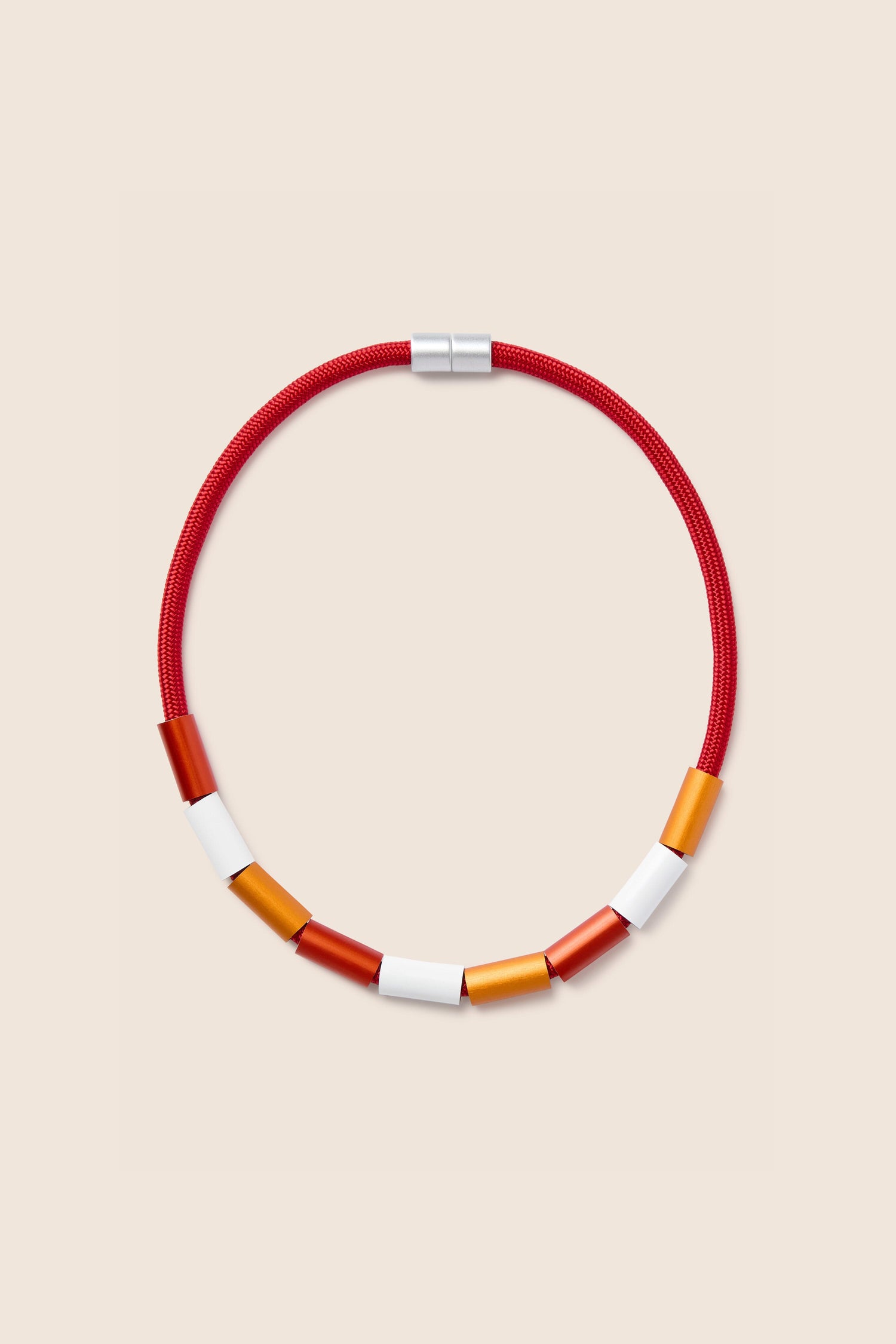 The Aluminium Cylinders Necklace by Christina Brampti showcases a contemporary design with a red cord and cylindrical beads in white, orange, and red, arranged in a symmetrical pattern.