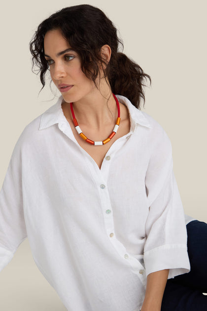 A woman with dark hair wearing a white button-up shirt and an eye-catching Aluminium Cylinders Necklace by Christina Brampti looks off to the side against a neutral background.