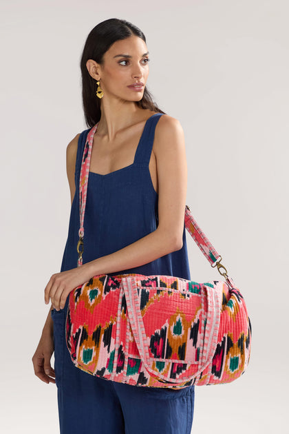 A woman wearing a dark blue sleeveless dress holds an Ikat Velvet Weekend Bag. She has long dark hair and is looking to the side, showcasing the bag's resist-dyeing technique that adds to its versatile design.