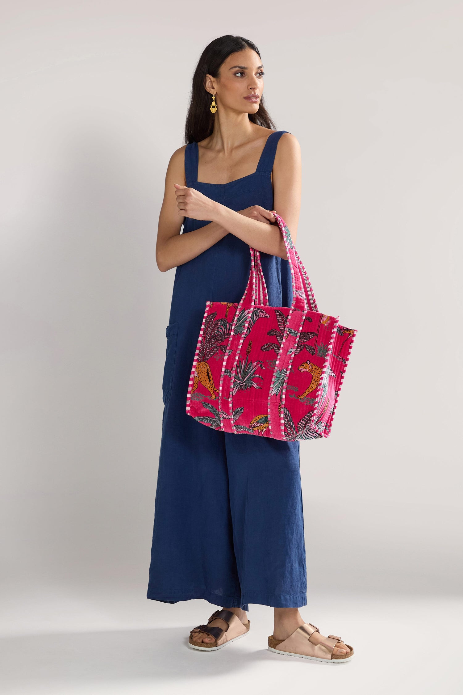 A woman in a blue jumpsuit and sandals holds a Jungle Print Velvet Bag.