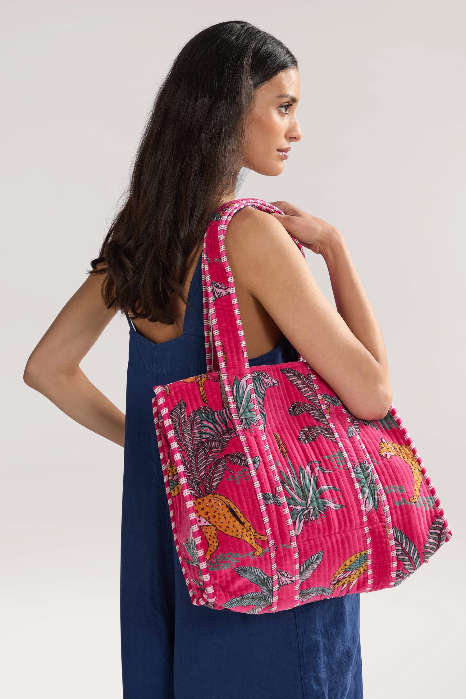 A woman with long dark hair is wearing a dark blue dress and carrying a large Jungle Print Velvet Bag. She is facing to the side and looking away from the camera.