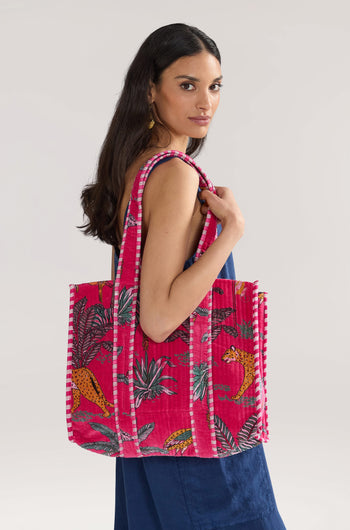 Woman with long dark hair carrying a Jungle Print Velvet Bag, dressed in a blue outfit. She is turned slightly to the side with a neutral expression.