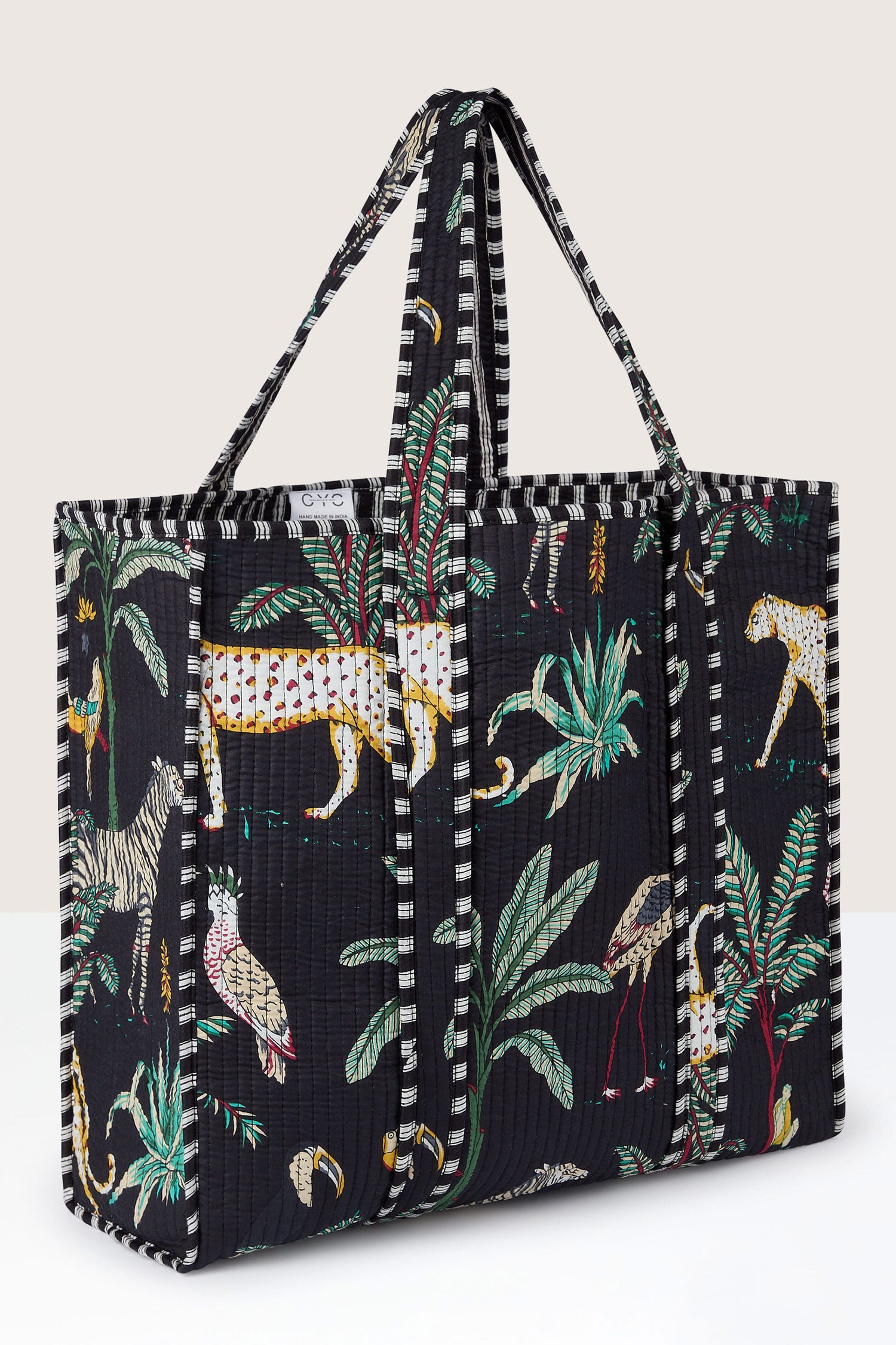 A large black Jungle Print Tote Bag with colorful animal and plant prints, featuring two striped handles, trim, and quilted fabric.