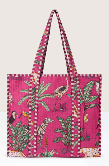 A Jungle Print Tote Bag from Conscious Yoga Collective features a colorful array of animals and plants, including zebras, birds, and palm leaves. The bag boasts long striped handles and a quilted fabric texture.