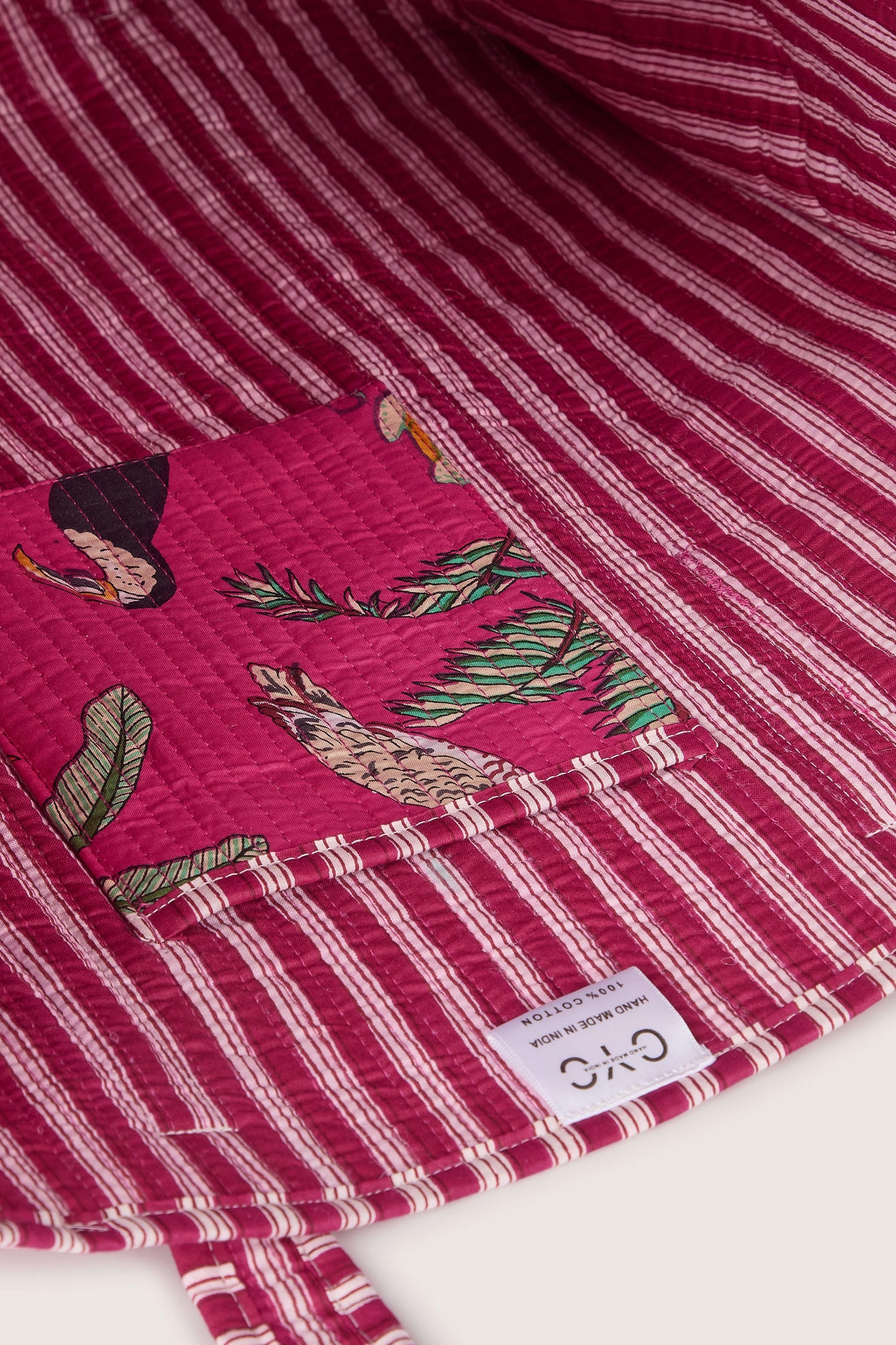 Close-up of a pink and white striped quilted fabric with a patch featuring bird and foliage illustrations. A label at the bottom reads "Jungle Print Tote Bag.