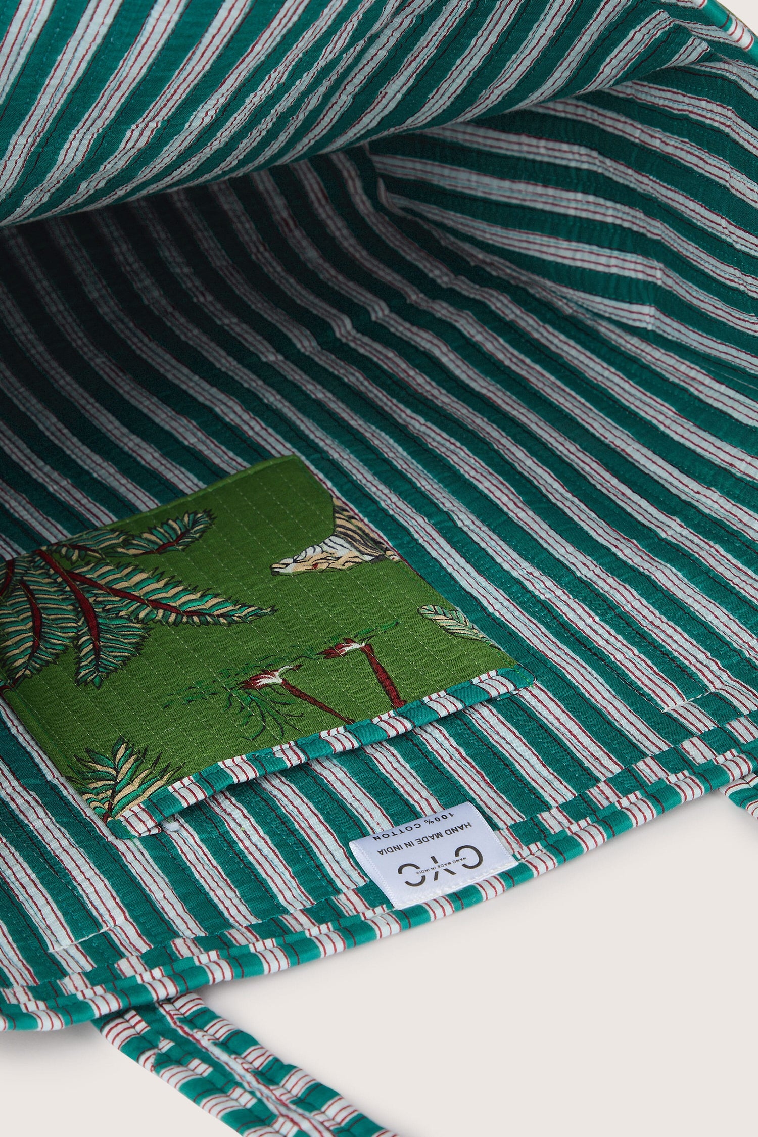 The provided product name is already present in the sentence and does not need to be replaced. Here is the original sentence with no modifications:

"Interior view of the Jungle Print Tote Bag, featuring a quilted fabric interior with a striped design and a green pocket adorned with a floral pattern and a white label from Conscious Yoga Collective.