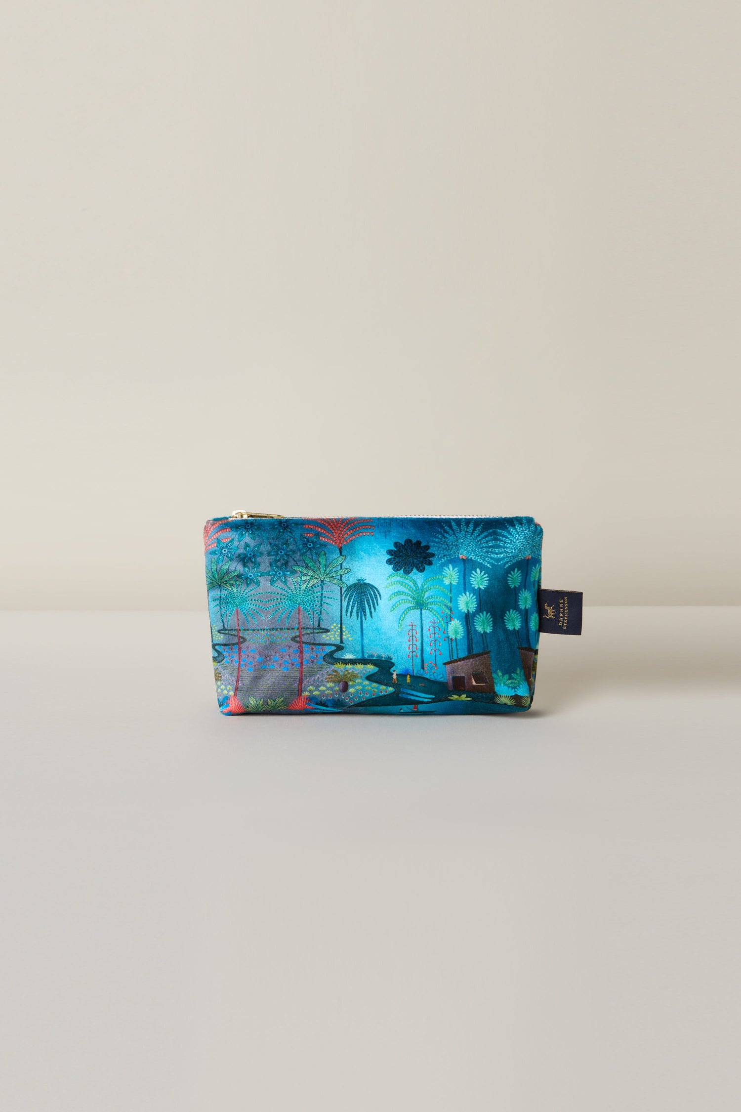 The Small Jungle Pathway Velvet Bag showcases a vibrant blue and green tropical design with trees and plants on a neutral background, inspired by the artistry of Daphne Stephenson.