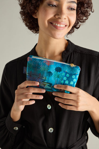 A person in a black top holds a Small Jungle Pathway Velvet Bag, showcasing its vibrant blue hue and nature-inspired design.