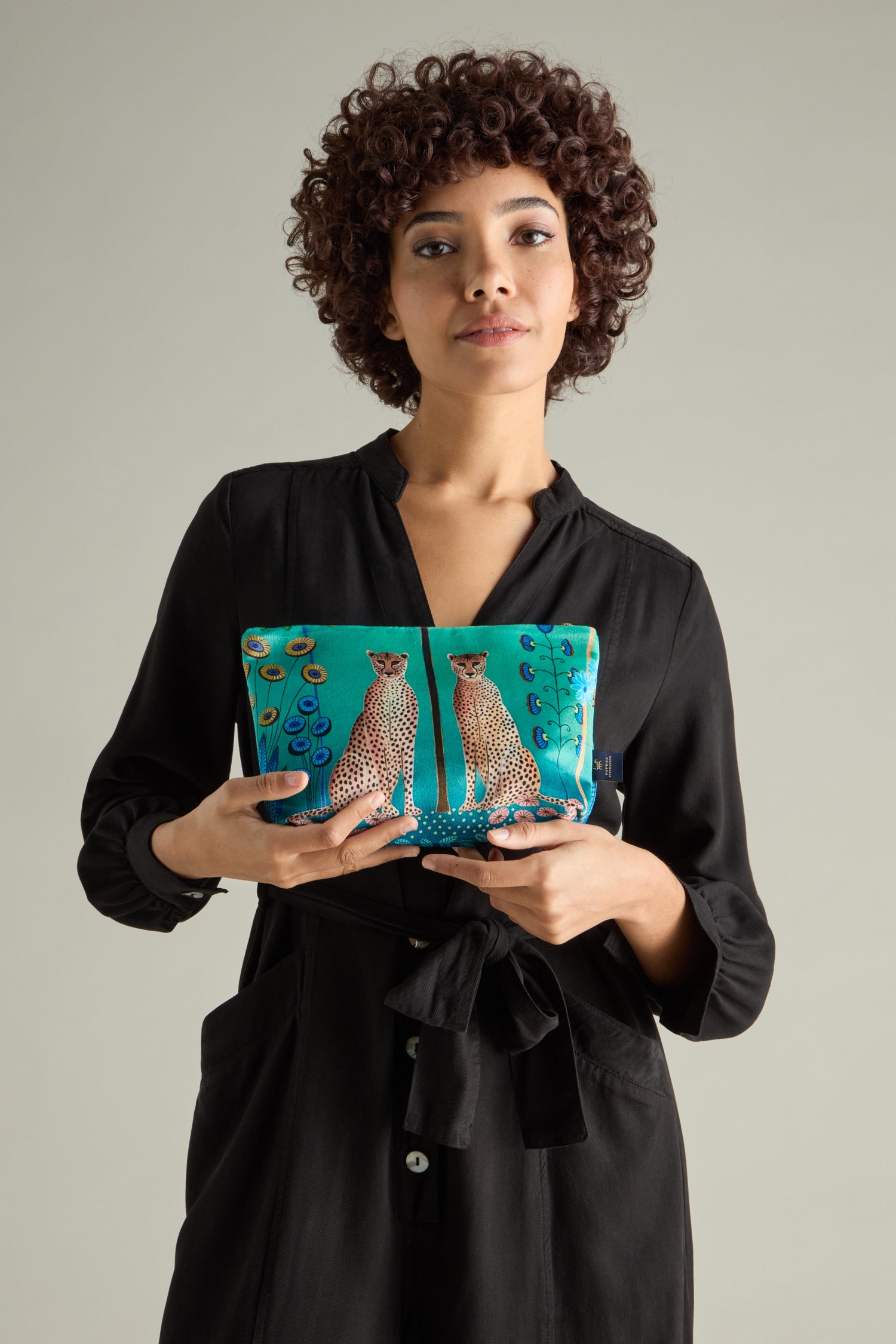 A person in a black dress elegantly holds a teal Large Sunshine Through My Window Velvet Bag adorned with the Cheetahs Design.