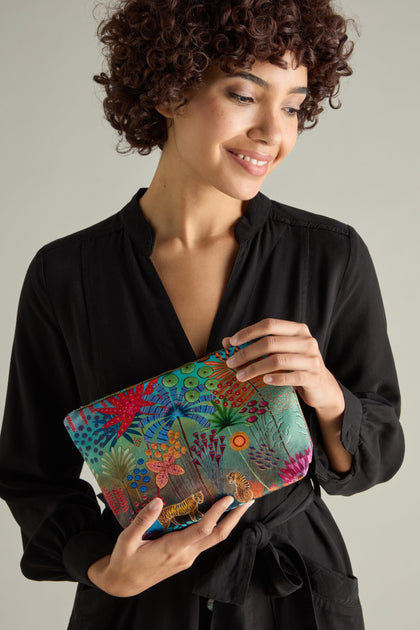 A person in a black dress elegantly holds the Large Tale of Two Tigers Velvet Bag, showcasing colorful floral and geometric motifs reminiscent of Daphne Stephenson's artistic flair.