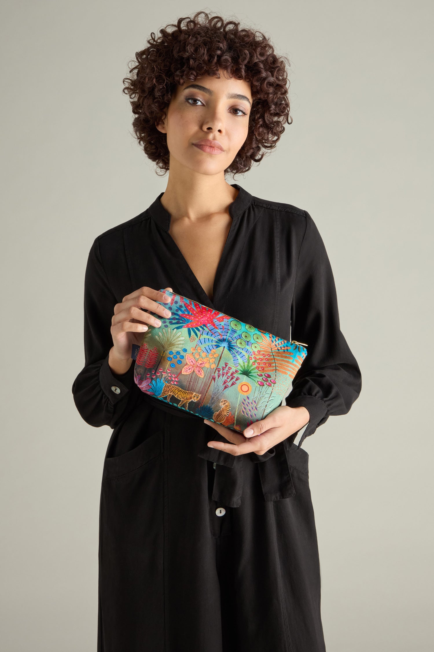 A person in a black dress holds a vibrant, patterned Large Tale of Two Tigers Velvet Bag against a neutral background, reminiscent of Daphne Stephenson's expressive style.