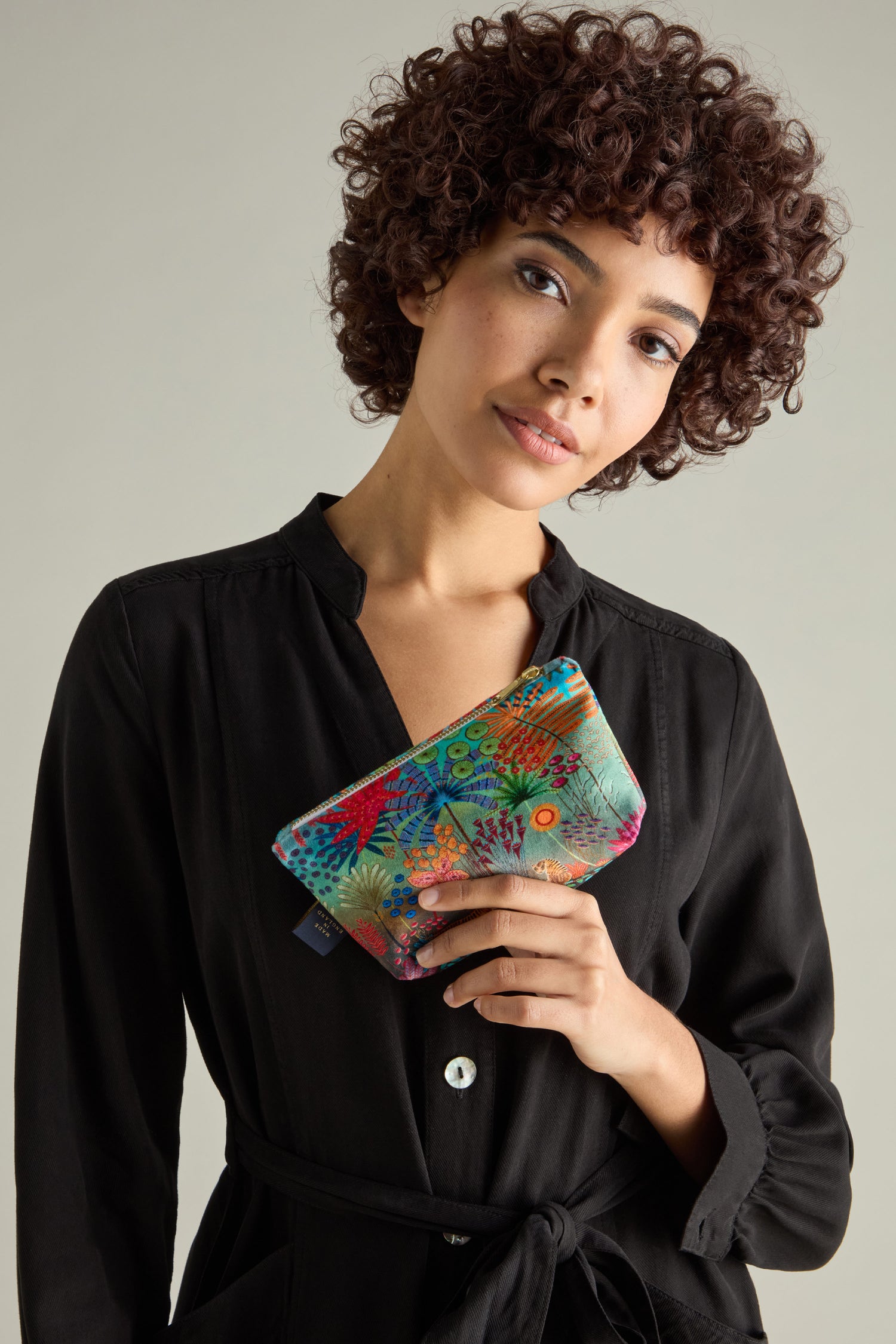 A person with curly hair holds a Small Tale of Two Tigers Velvet Bag while wearing a black collared dress, capturing the enchanting style reminiscent of Daphne Stephenson.