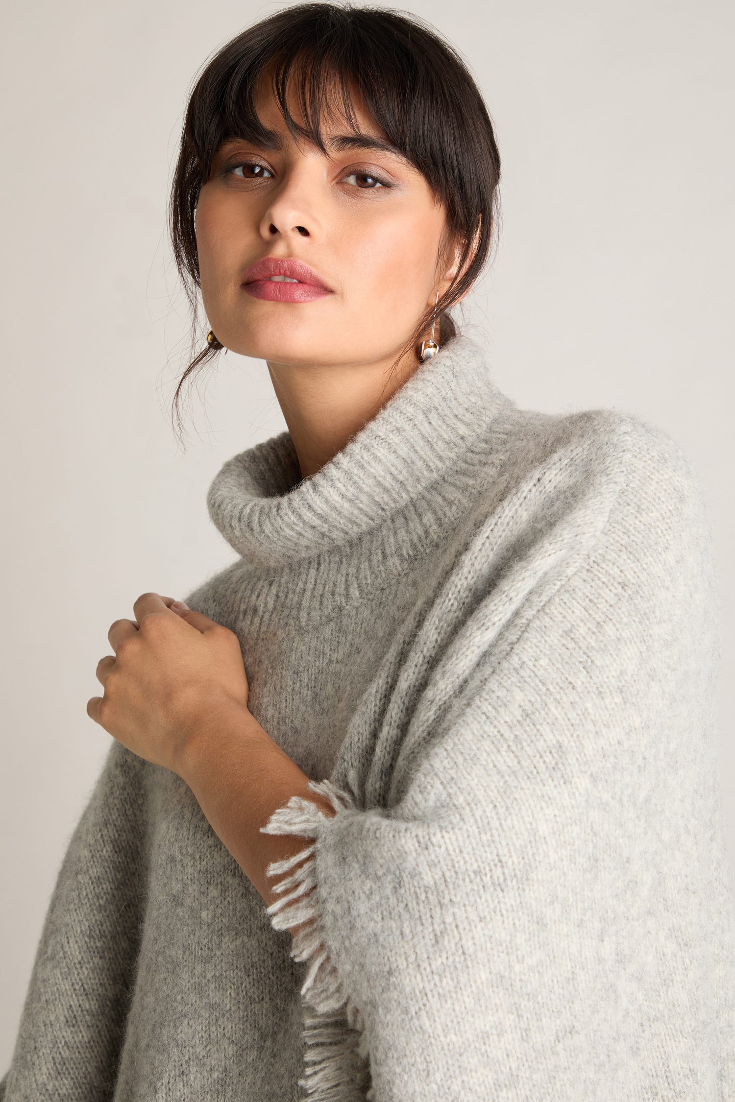 A person in a Cashmere And Alpaca Poncho, featuring grey wool and fringe details on the sleeves, exuding both luxury and comfort, poses against a plain background.