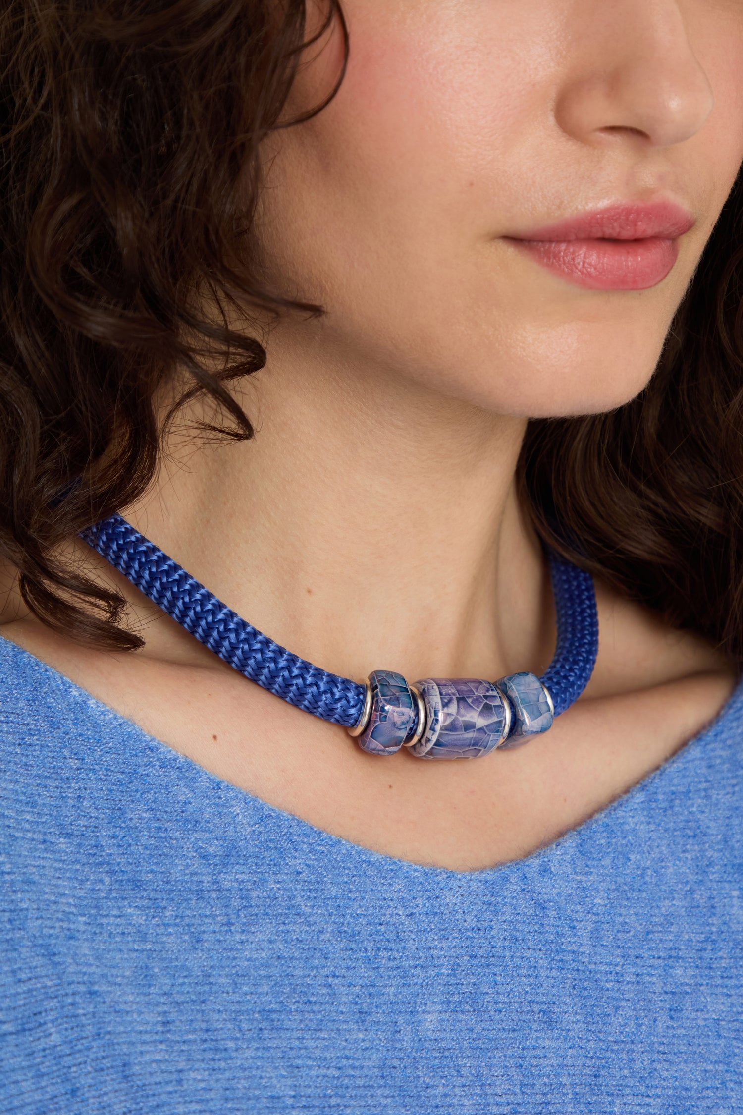 A woman wears a blue top and the Triple Marble Bead Short Cord Necklace—a Sahara exclusive, braided blue choker with three large statement beads.