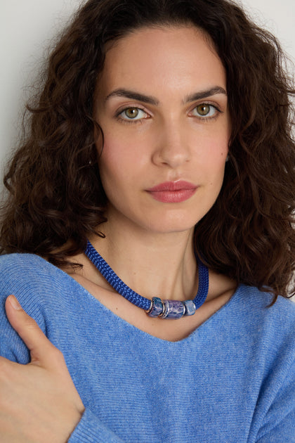 Woman with curly brown hair wearing a blue sweater and the Triple Marble Bead Short Cord Necklace, featuring silver and transparent details, posing against a plain background.