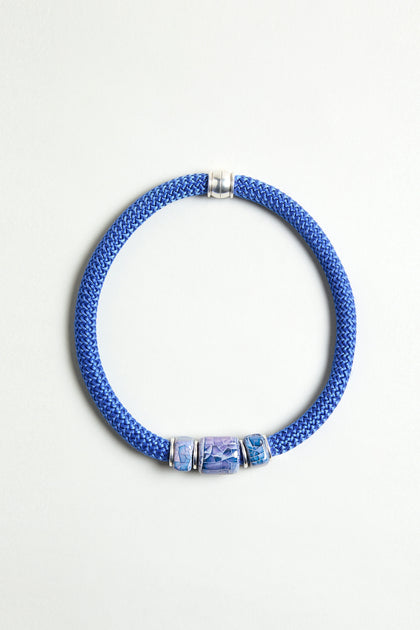 The Triple Marble Bead Short Cord Necklace features three patterned blue and silver cylindrical beads, silver accents, and a chunky cord design, beautifully displayed on a light background.