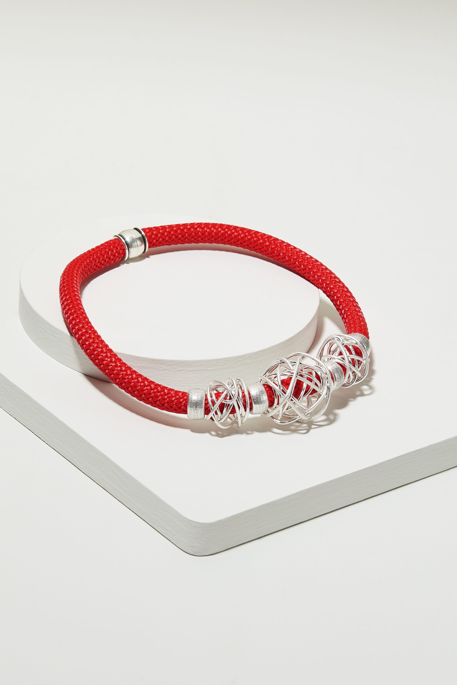 A red Triple Squiggle Necklace with sculpted silver beads on a white surface.