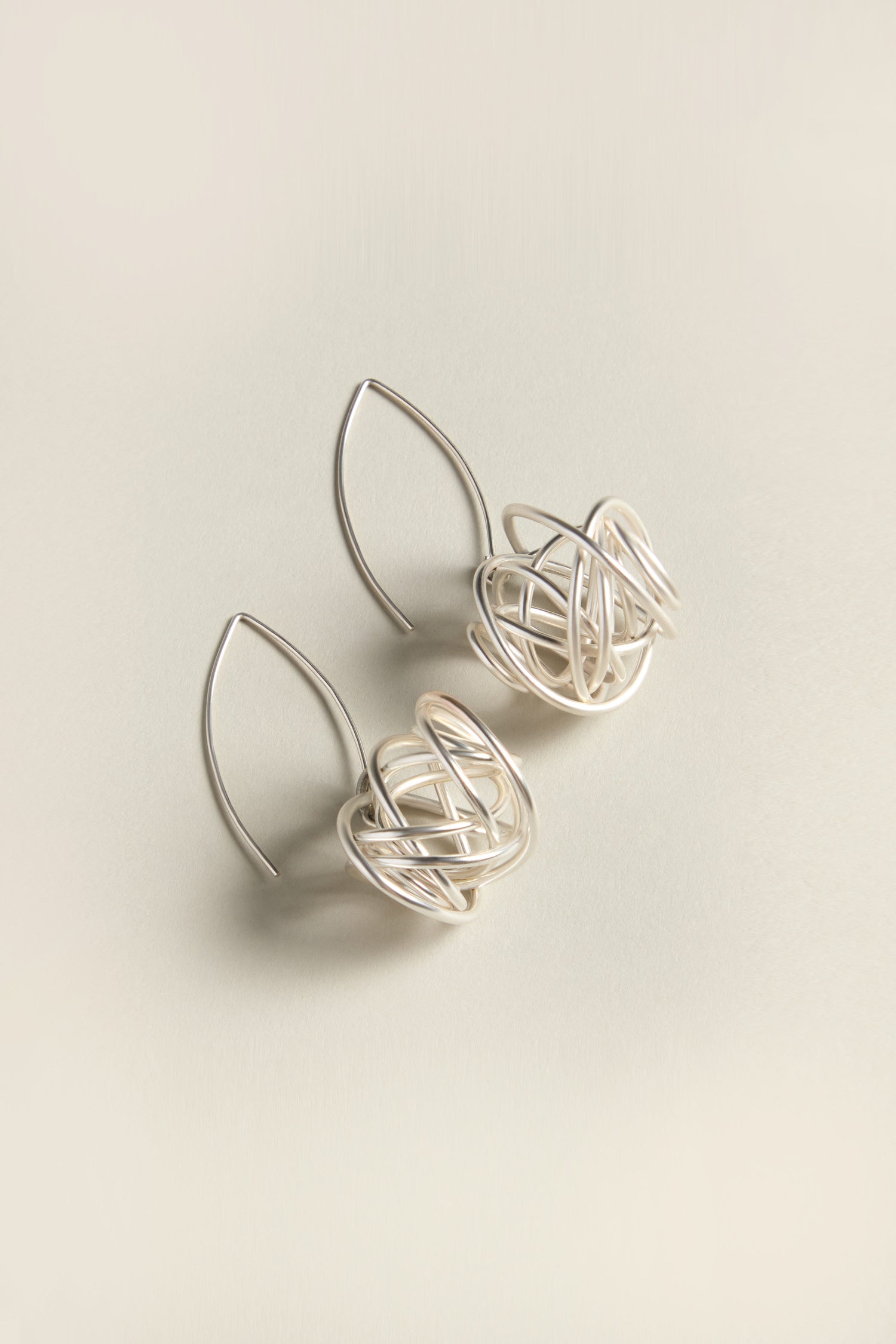 The Silver Scribble Earrings consist of looped, wire-like designs set against a neutral background, creating a modern jewelry piece that makes an artistic statement.