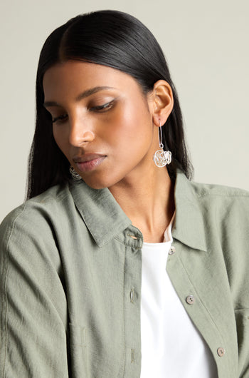 A woman, adorned in a green shirt and white top, makes an artistic statement with the Silver Scribble Earrings. She gazes downward against a neutral background, capturing the elegance of Etnika jewelry.