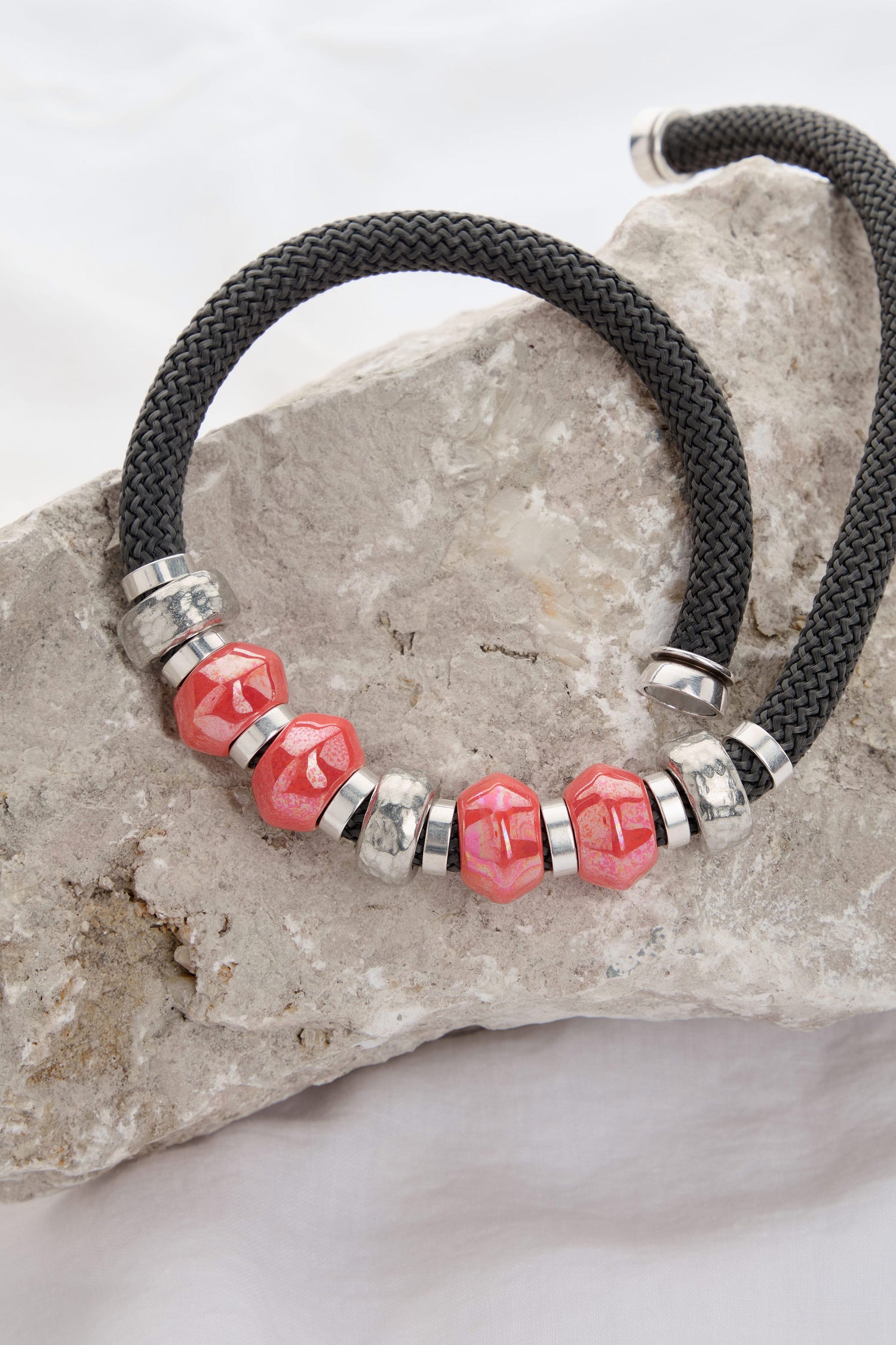 A Coral Bead Cord Necklace displayed on a rough, light-colored rock surface makes for a striking statement piece.