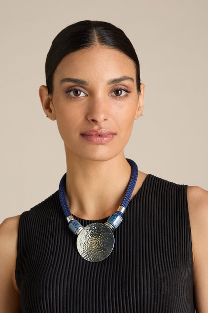 A woman wearing a black sleeveless top showcases an Etnika jewellery Hammered Sphere Cord Necklace, featuring a bold blue pendant that perfectly complements her ensemble.