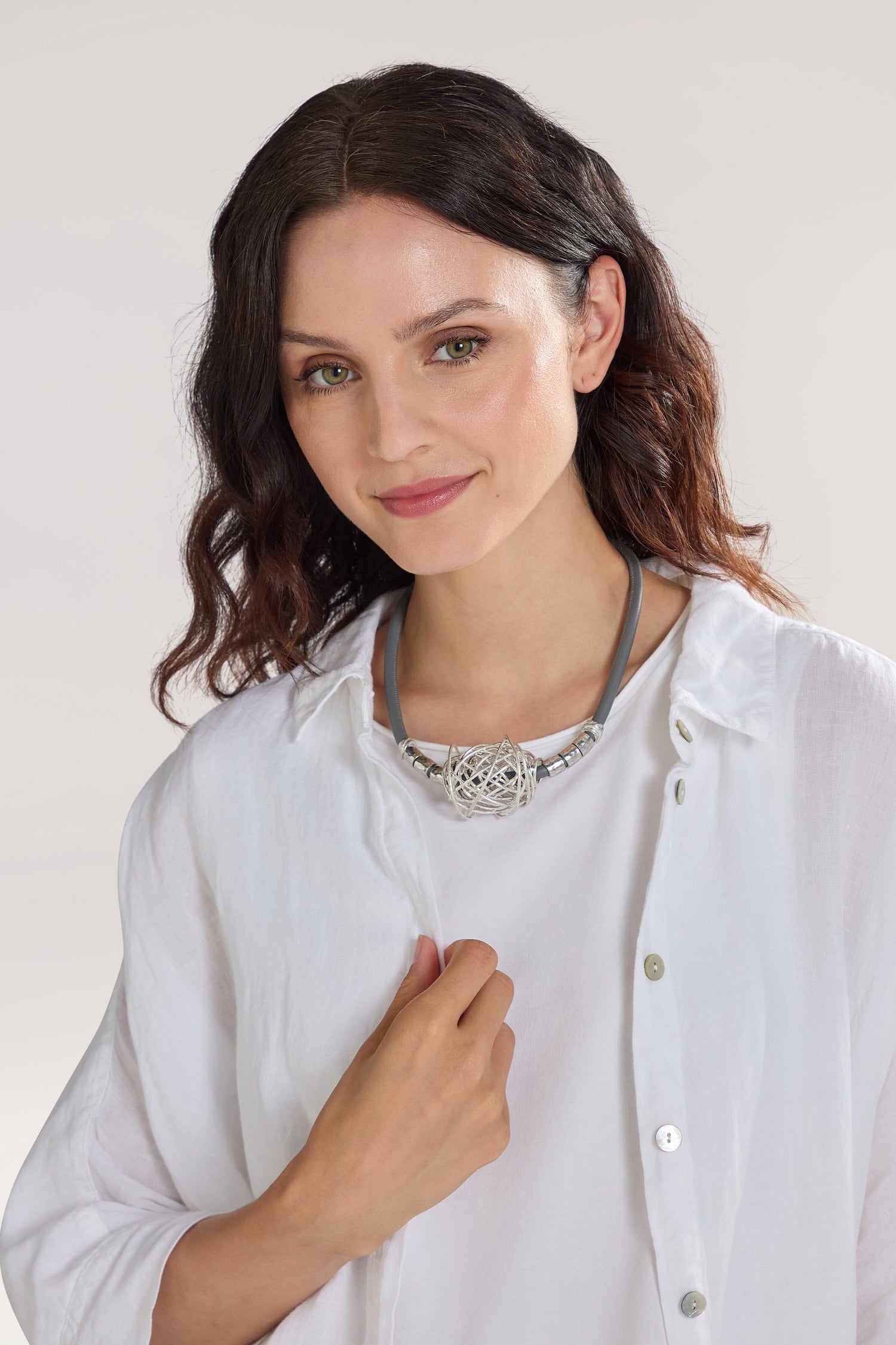 A woman with wavy hair wearing a white blouse and a Scribble Bead Leather Cord Necklace looks at the camera with a neutral expression.