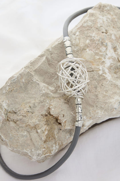 A Scribble Bead Leather Cord Necklace is artfully displayed on a large, textured rock against a white background, showcasing Etnika-inspired design.