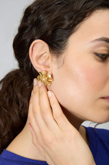 A woman with dark hair wears Gold Plated Flower Pearl Earrings, each featuring a pearl center, as she gently touches her ear.