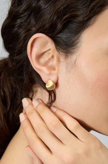 A close-up of a woman's ear wearing Gold Plated Mini Pebble Earrings, her hand gently resting on her neck.
