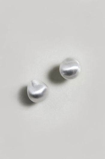 The Mini Silver Pebble Earrings, featuring a round, irregular organic shape and a silver-tone finish, are displayed on a plain light-colored surface.