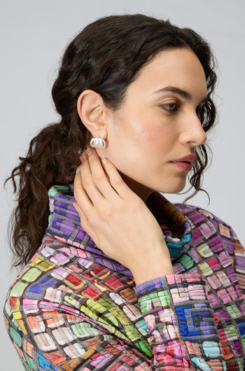Woman with wavy brown hair, shown in profile wearing a multicolored textured top and Silver Vortex Earrings, her hand gently touching her ear.