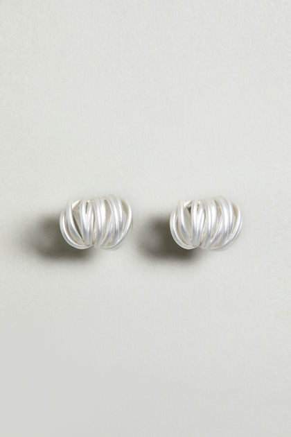The Silver Vortex Earrings are sculptural, silver studs with a spiral shape, showcased against a simple light background.