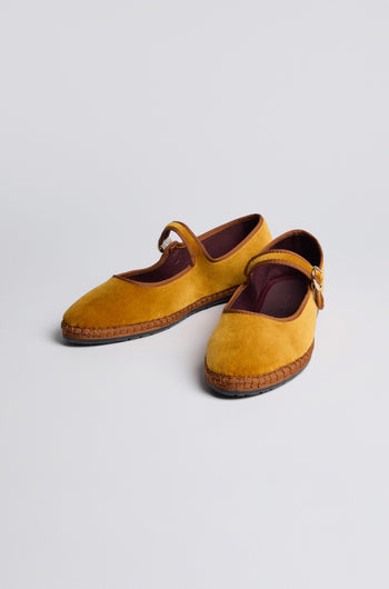 Mustard Mary Jane Velvet Shoes feature brown straps and stitching details, crafted sustainably in mustard yellow velvet, displayed on a plain light background.