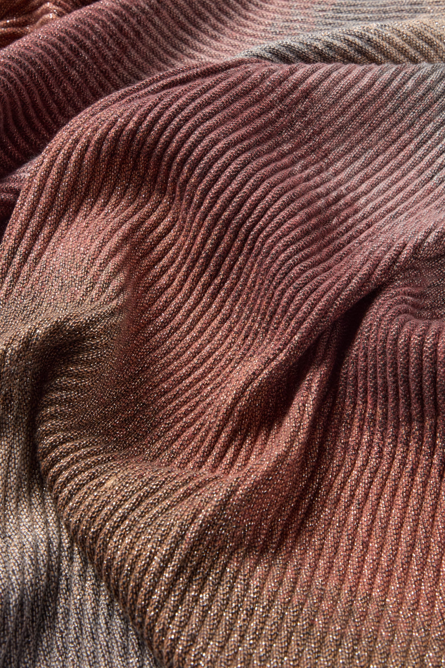 Close-up of a textured Stardust Scarf by Fraas featuring a gradient pattern that transitions from dark red to earthy tones. The fabric exhibits a ribbed surface and appears to be draped or gathered.