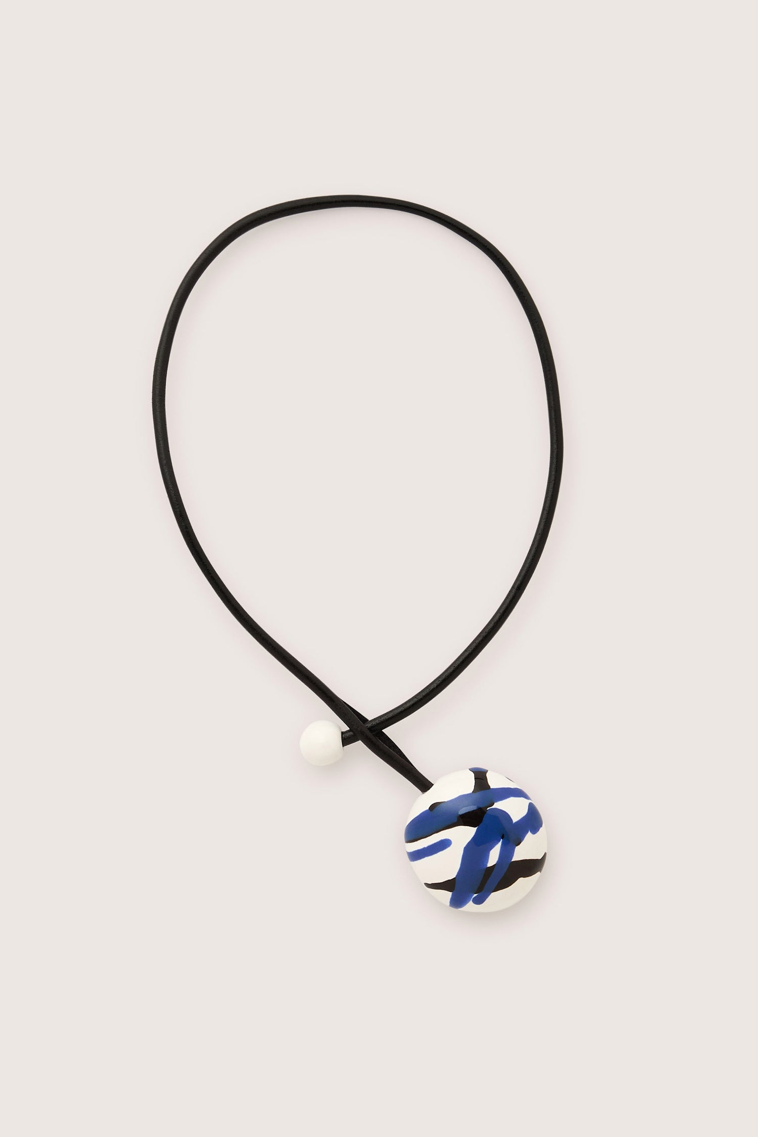 The Handmade Ceramic Painted Bead Necklace highlights traditional craftsmanship through a modern lens, with its black cord and pendant adorned with abstract blue and black patterns, complemented by a small white bead.