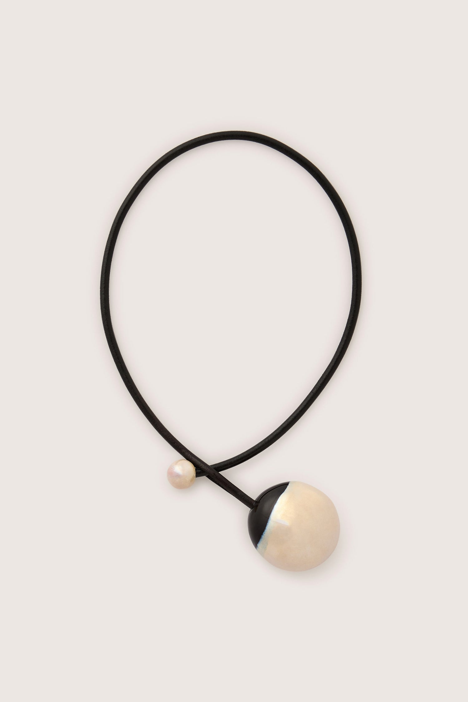 The Handmade Ceramic Pearl Bead Necklace showcases exquisite artisanal craftsmanship with a black cord and two spherical pendants: one is large, partially black and white, while the other is small and pearl-like.