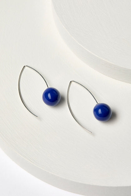 The Handmade Ceramic Bead Earrings highlight spherical blue handmade ceramic beads set on 925 sterling silver wire, elegantly showcased against a white background.