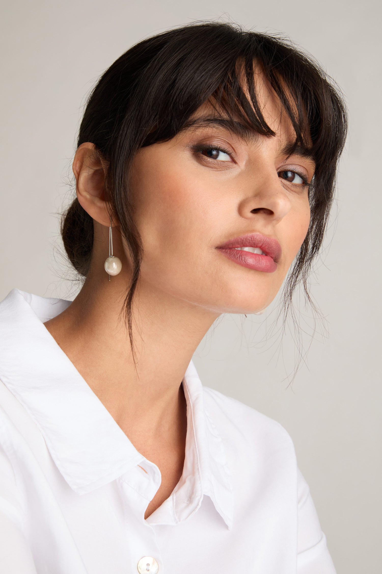 A woman with dark hair and bangs wears a white shirt and Handmade Ceramic Bead Earrings, highlighted by artisanal craftsmanship, looking slightly to the side with a neutral expression.