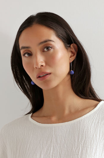Woman with long dark hair wears a textured white top and Handmade Ceramic Bead Earrings, featuring a sculptural twist design, as she looks at the camera against a plain light background.