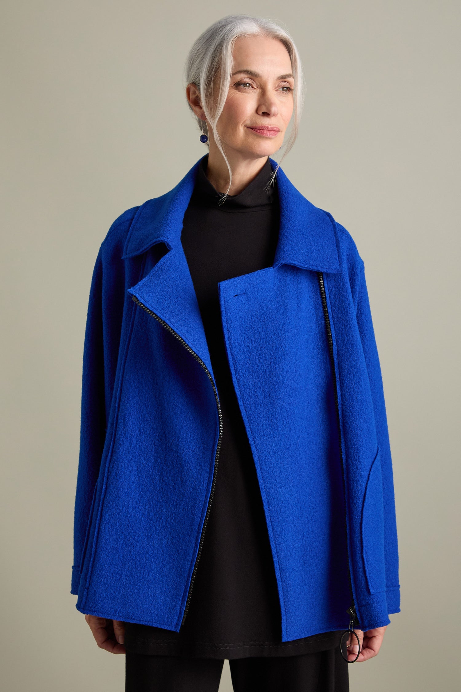 An older adult with gray hair is wearing a Boiled Wool Zip Boxy Jacket in royal blue over a black outfit, standing against a plain background.