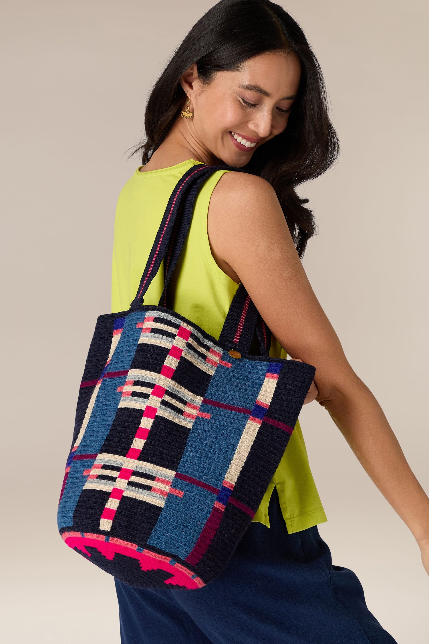 Woman smiling over her shoulder, holding a Handcrafted Cala Tote Bag with colorful geometric patterns made using traditional techniques. She is wearing a lime green top.