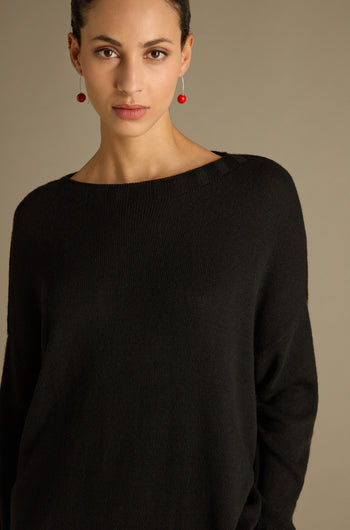 A person elegantly wearing a Merino Blend Crop Jumper and red earrings stands against a neutral background.