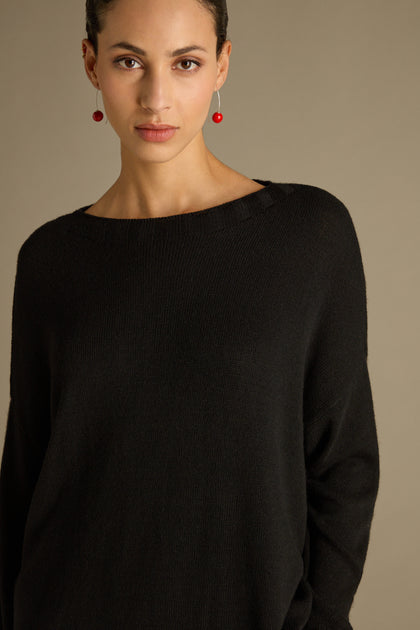 A person elegantly wearing a Merino Blend Crop Jumper and red earrings stands against a neutral background.