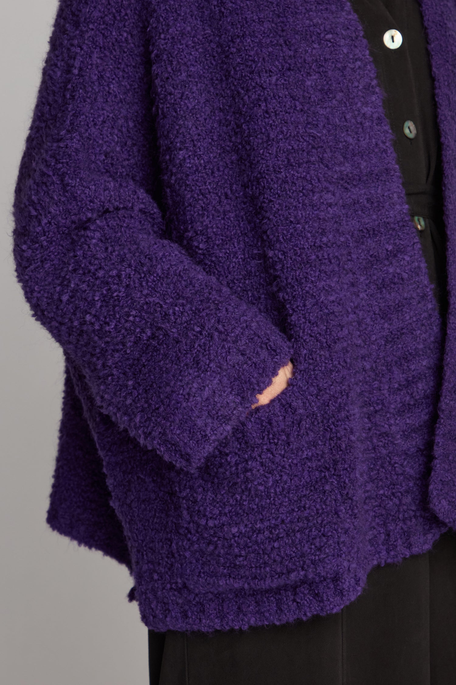 A person is wearing a Boucle Knit Cable Trim Cardi in dark purple textured wool with large pockets, over a black outfit.