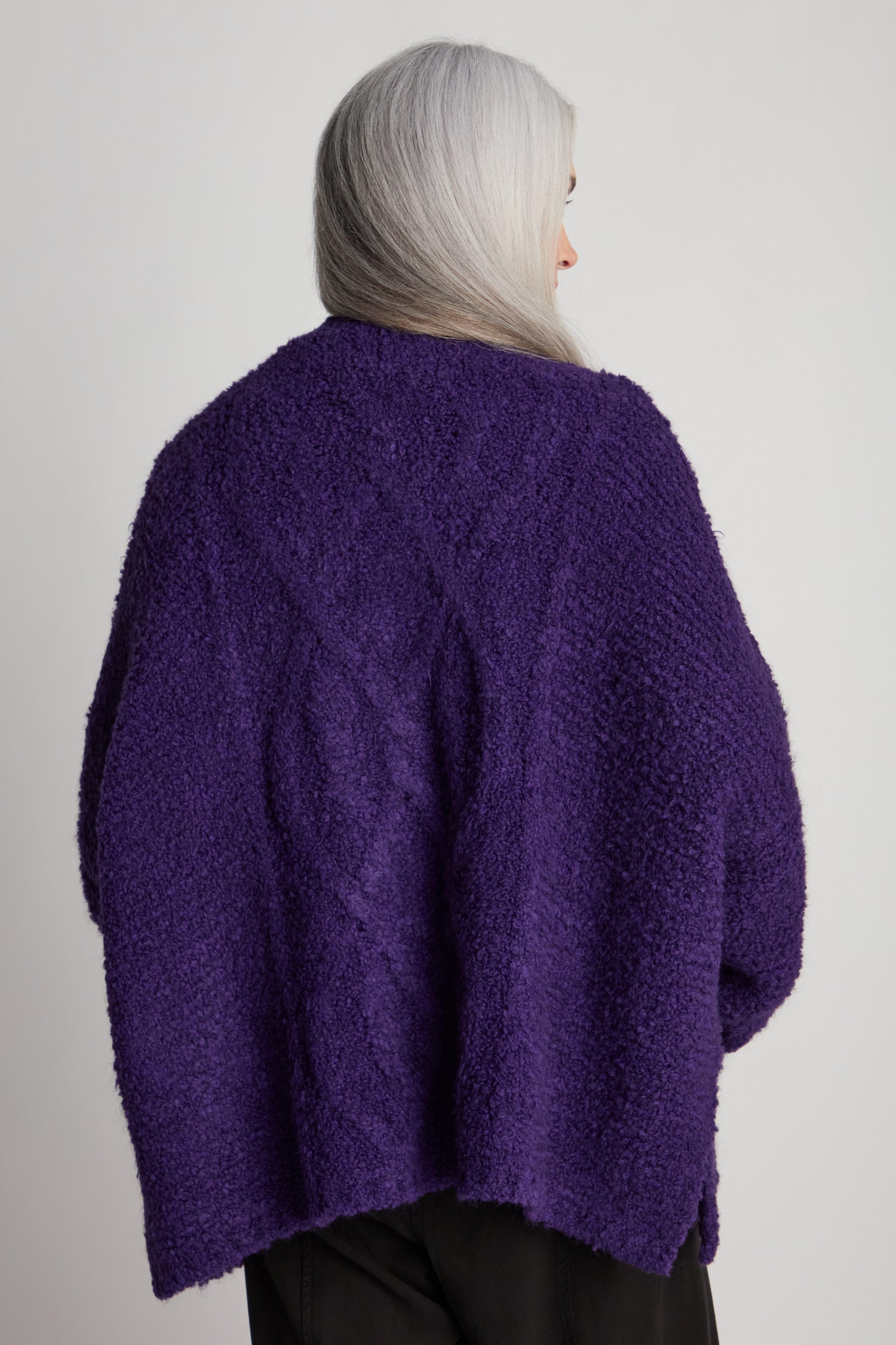 Person with long gray hair wearing a Boucle Knit Cable Trim Cardi in purple, photographed from behind.