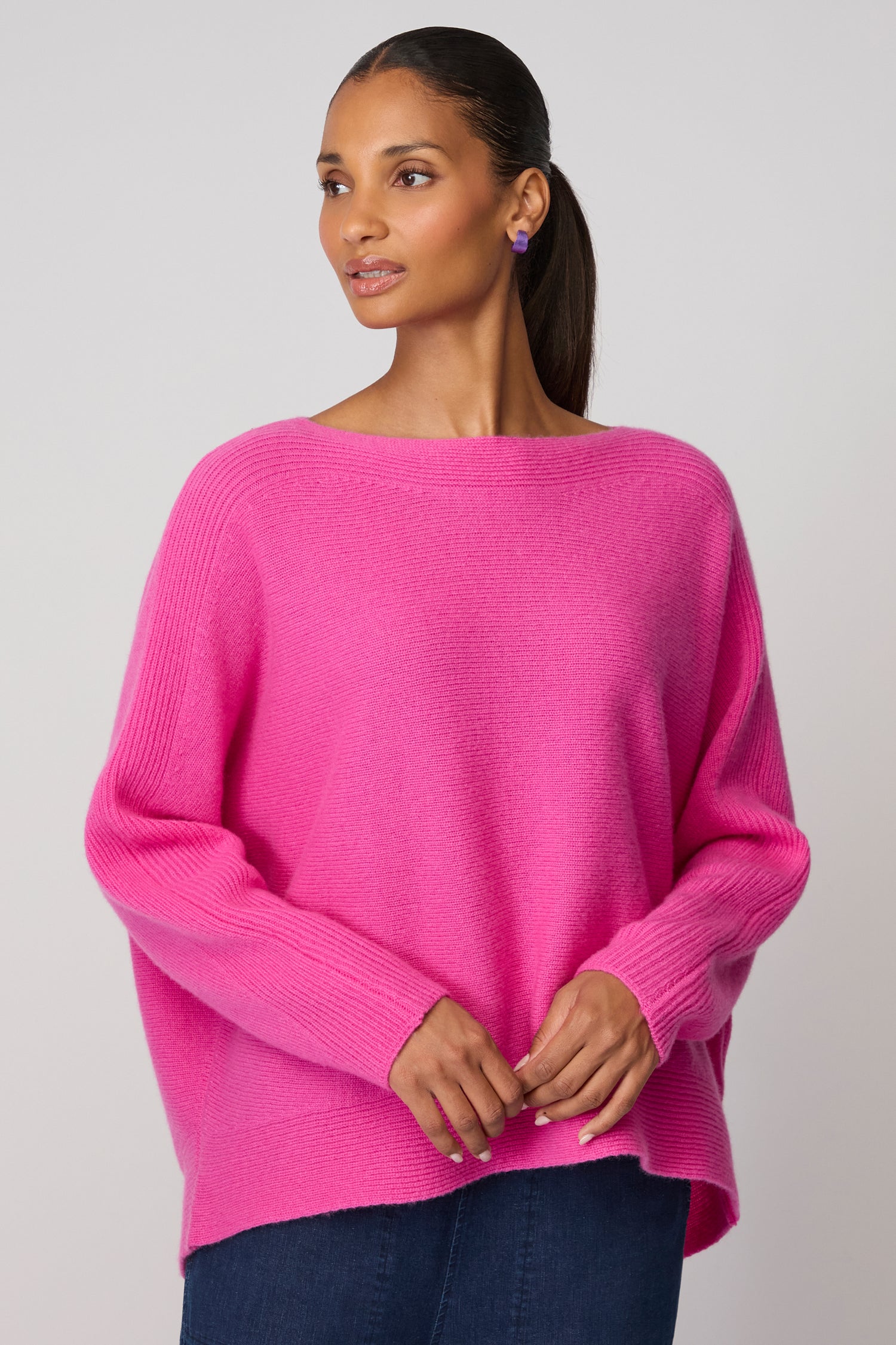 A woman models the Merino Rib Detail Jumper in bright pink with dark pants, standing slightly side-on against a plain background to showcase this stylish women's knitwear.
