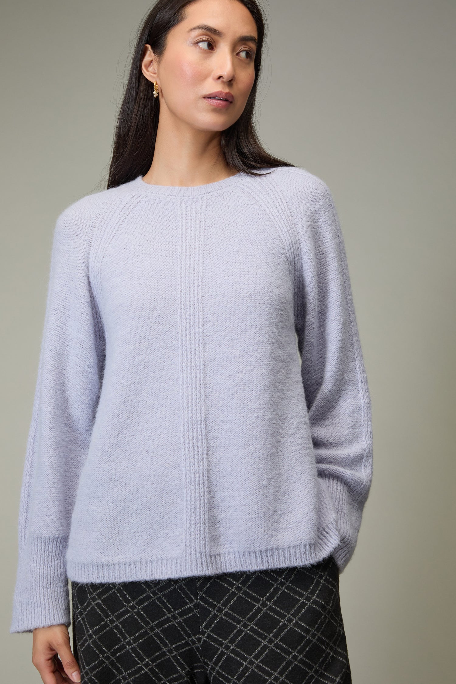 A woman wearing the Alpaca Blend Seam Detail Jumper in light purple and dark plaid pants stands against a plain background, looking to the side.